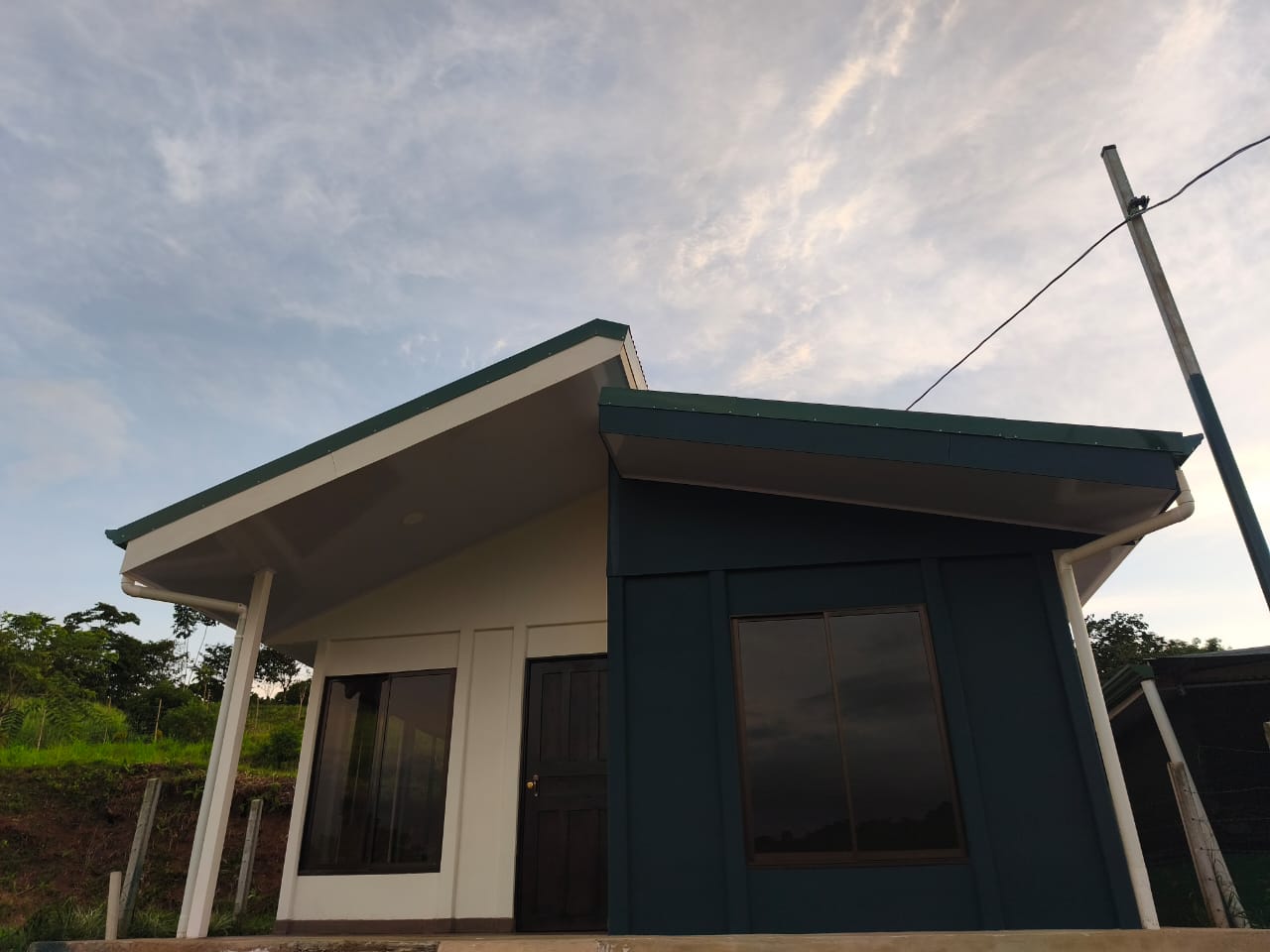 Vista frontal de casa prefabricada blanca con techo verde y ventanas de aluminio negro